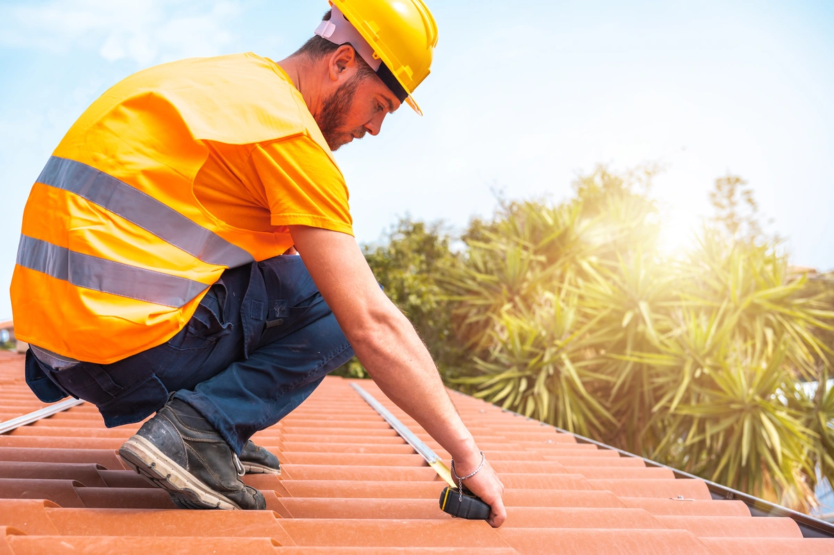 roof tech in a yellow vest measuring red roof