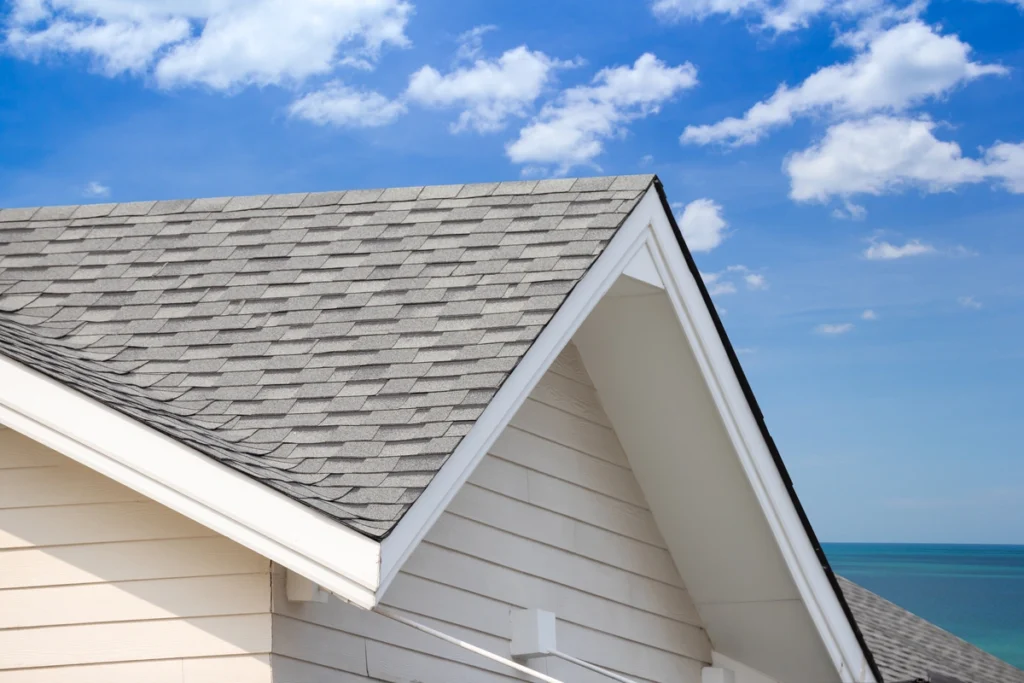 roofing on a cream colored house with blue cloudy sky in the background